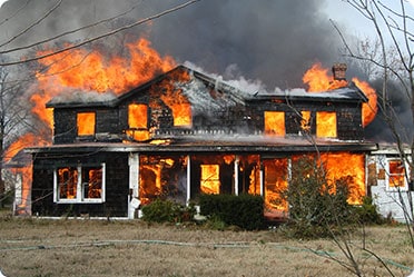 A blazing house with flames bursting out of the windows in a destructive fire - The Lawler Group