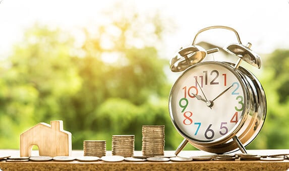 A clock and coins on a table with two houses, representing financial planning opportunities. - The Lawler Group